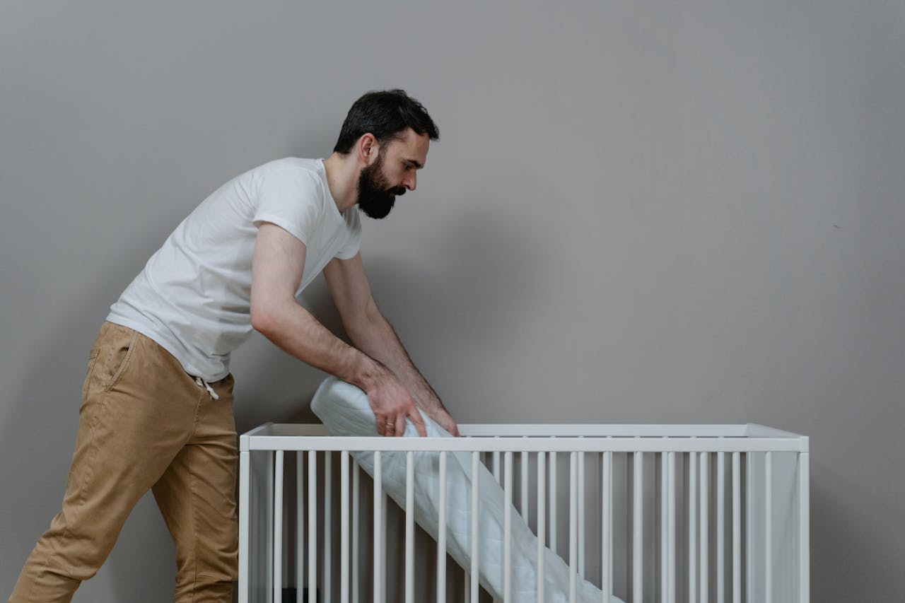 A bearded man setting up a crib in a minimalistic nursery room.